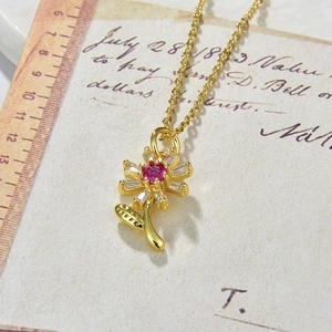 Close-up of golden sunflower pendant with pink and white zircon beside a vintage ruler