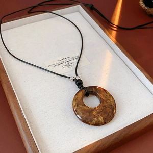Detail of amber resin ring pendant with leopard cloud texture on black cord necklace