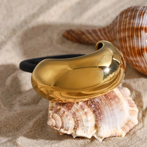 Elegant gold metal pod-shaped hair tie with black elastic band on a seashell at beach
