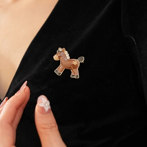 Detail view of a gold-toned pony brooch with brown enamel and rhinestones on black velvet