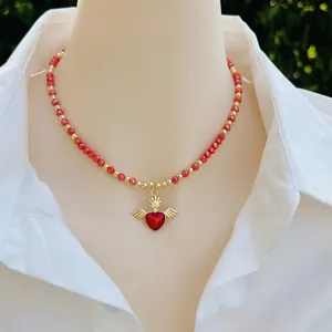 Handmade beaded red and gold necklace with winged heart pendant worn on white shirt