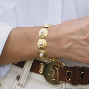 Primer plano de una pulsera dorada vintage con discos metálicos y perlas en la muñeca