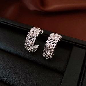 Detailed close-up of silver hollow leaf earrings on a premium black leather jewelry box