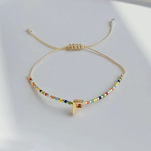 Detail eines böhmischen Miyuki-Perlenarmbands mit verstellbarem Knoten und goldenem Buchstaben F