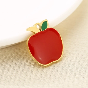 Detail of red apple pendant charm with gold plating and green leaf on beige fabric