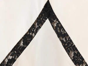 Detail von cremefarbenem Satin mit exquisiter schwarzer Spitze und Stickerei-Verzierung