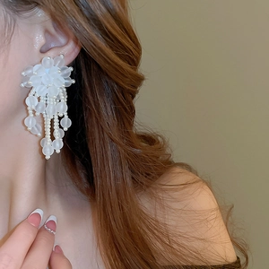 Detail of white floral tassel earrings with frosted acrylic petals and pearls on a model