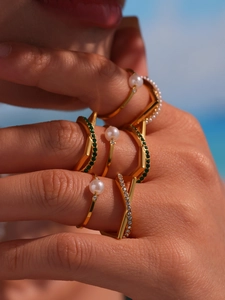 Close-up of dual-layer gold plated ring with white pearls and green gemstones on hand