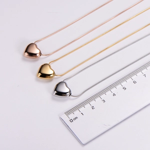 Trois colliers avec pendentif cœur en titane montrés avec une règle pour mesurer la taille