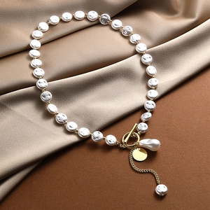 Detail of baroque pearl necklace with gold T-bar clasp on champagne silk fabric