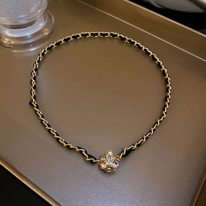 Détail de la chaîne dorée tressée de cuir noir avec pendentif sphère en cristal