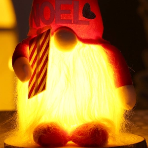 Close-up of glowing Christmas gnome with NOEL hat and warm LED light on wooden base