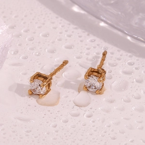 Macro view of gold studs with clear round zircon set in a four-prong mount on white background