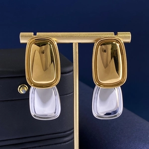 Detailed close-up of golden titanium steel earrings with transparent acrylic tag pendants