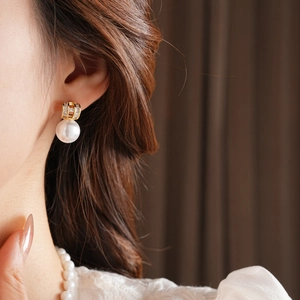 Close-up of gold plated pearl earrings with crystals worn by a model in soft lighting