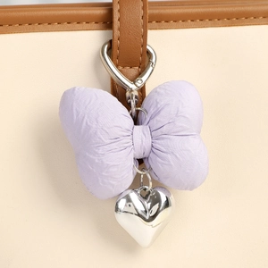 Detail of a purple fabric bow charm with a silver heart pendant on a leather handbag