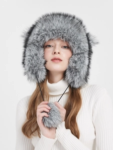 Detailed view of grey faux fur trapper hat with soft earflaps and plush hanging pom-poms
