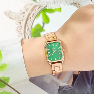 Détail d'une montre carrée or rose avec cadran vert et diamants au poignet du mannequin