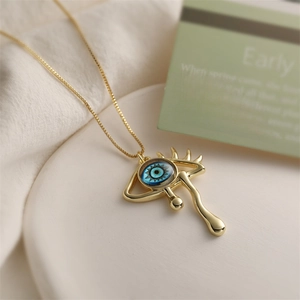 Detailed shot of golden Evil Eye pendant with blue stone and teardrop on white plate