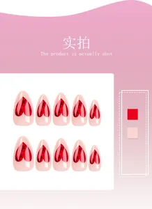 Detail view of 10 almond-shaped press-on nails with red heart patterns on nude pink base