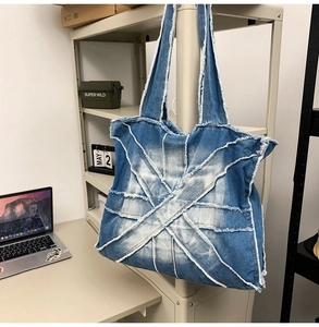 Detailed view of frayed edges on a blue denim tote bag with textured patchwork design