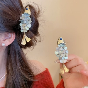 Detail shot of fish-shaped hair clip with iridescent shell scales and golden metal finish