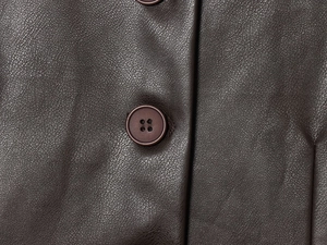 Vue détaillée de la texture en similicuir marron foncé et du bouton sur la veste