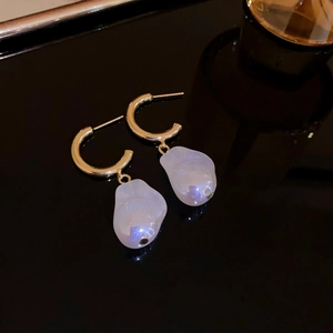 Detail of gold star earrings with baroque pearl drops on a black reflective surface