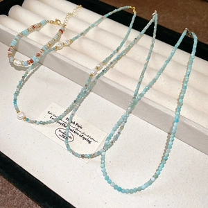 Detail of layered geometric pearl necklace with light blue stones and gold clasp