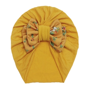 Detail of baby girl mustard yellow turban hat with a floral pattern bow on white background