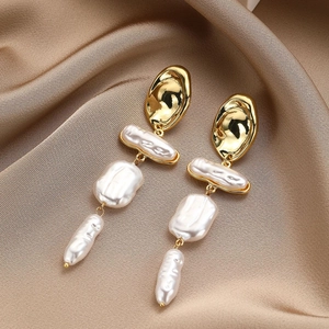 Detailed macro view of long baroque pearl earrings with gold metal on champagne silk