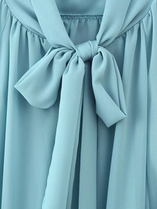 Detail shot of a light blue chiffon blouse showing the neck tie bow and pleated texture