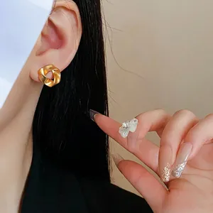 Golden twisted round stud earrings in matte silk finish on female model's earlobe