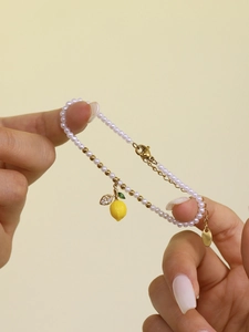 Detail of beaded bracelet with white pearls, golden beads and yellow lemon pendant