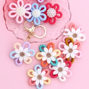 Colorful woven daisy and sunflower keychains with golden hooks on pink background