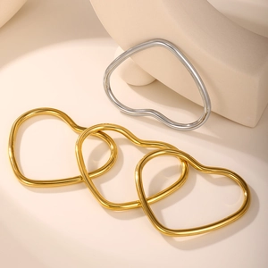 Detail of minimalist 18k gold and silver heart-shaped bangles on geometric props