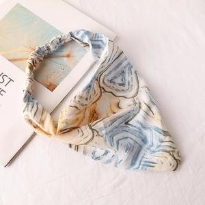 Detail of blue and yellow tie-dye chiffon headscarf with elastic band on white fabric