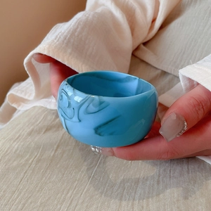 Close-up of wide acrylic bangle featuring a blue marble texture held by a model