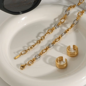 Detail view of two-tone stainless steel chain and gold multi-layer ear cuffs on a tray