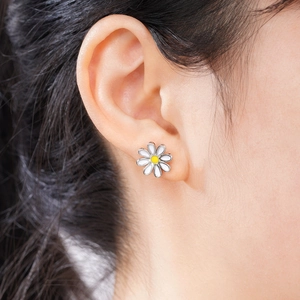Close-up of a white daisy stud earring worn on the ear showing delicate floral details