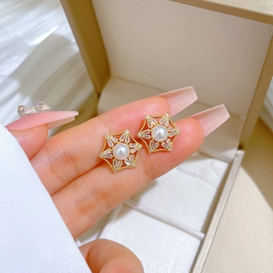 Detail of gold hex star stud earrings featuring a central white pearl and clear zircons