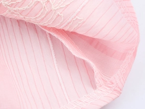 Detail von rosa gestreiftem Stoff mit weißer Stickerei und hochwertiger Naht