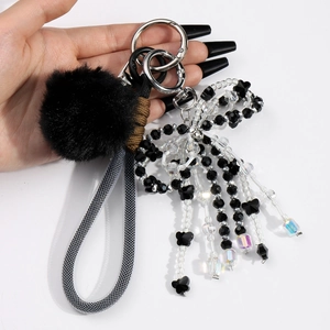 Chic black pompom keychain with crystal bow and mesh lanyard held in hand