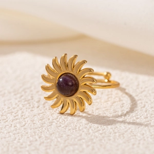 Macro detail of a gold sunburst ring featuring a deep purple gemstone on a textured surface