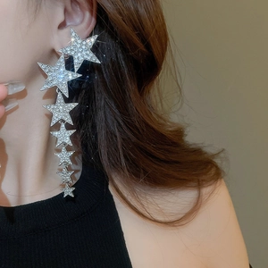 Silver dangling earrings with rhinestone star pendants worn by a model on warm background