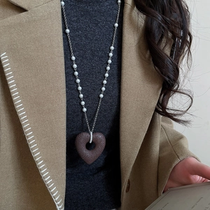 Detail of beaded necklace with brown heart pendant and pearls on a grey sweater