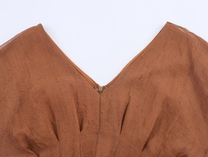 Macro shot of V-neckline on dark brown dress featuring invisible zipper and pleated texture