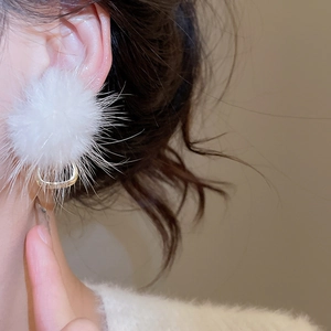 Close-up of elegant white plush pom-pom earring with golden U-shaped clasp on ear