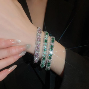 Close-up of stacked silver bracelets with pink and green zircon stones on model wrist