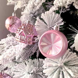 Close-up of pink plastic Christmas ornaments in ball and house shapes on snowy tree branches